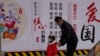 一名男子带着小女孩走过北京街头一面中国政府的宣传社会主义核心价值观的宣传墙。（2021年3月7日）