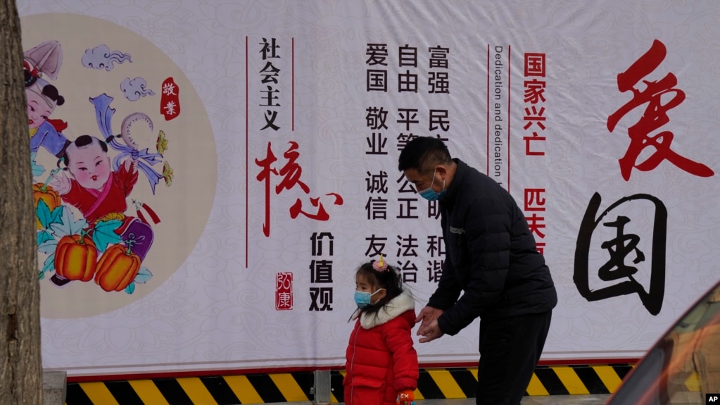 一名男子带着小女孩走过北京街头一面中国政府的宣传社会主义核心价值观的宣传墙。（2021年3月7日）(photo:VOA)