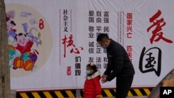 一名男子带着小女孩走过北京街头一面中国政府的宣传社会主义核心价值观的宣传墙。（2021年3月7日）