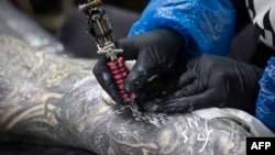 A client has artwork added to his leg at Dragon Tattoo and Body Piercing in Sheffield, England, July 13, 2020. “The dragon always comes with a lot of good meanings, especially for Asian people," says Hong Kong tattoo artist Marcus Yuen. 
