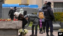 Police officers patrol an area as people lay flowers at a large stone from the Solovetsky islands, where the first camp of the Gulag political prison system was established, near the building of the Federal Security Service in Moscow, Oct. 29, 2023.