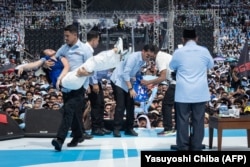 Seorang pendukung paslon Prabowo Subianto dan Gibran Rakabuming Raka yang pingsan digotong oleh petugas keamanan saat Prabowo sedang berpidato dalam kampanye akbar di Stadion Gelora Bung Karno, Jakarta, 10 Februari 2024. (Foto: Yasuyoshi Chiba/AFP)