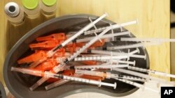 FILE - Syringes with COVID-19 vaccine sit ready for use in New Orleans, Jan. 25, 2022. COVID-19 hospital admissions have inched upward in the U.S. since early July; an updated vaccine is still months away.