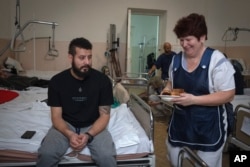 FILE - A nurse brings lunch for a wounded professional soldier from Medellín, Colombia, who goes by the call sign of Checho, 32, in a hospital in Ukraine, Dec. 20, 2023.