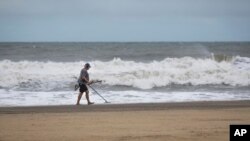 A man uses a metal detector on the Virginia Beach oceanfront during Tropical Storm Ophelia on Sept. 23, 2023, in Virginia Beach, Va.