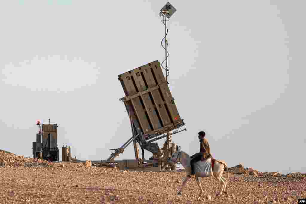 A boy rides a donkey near one of the batteries of Israel&#39;s Iron Dome missile defense system at a village not recognized by Israeli authorities in the southern Negev desert.