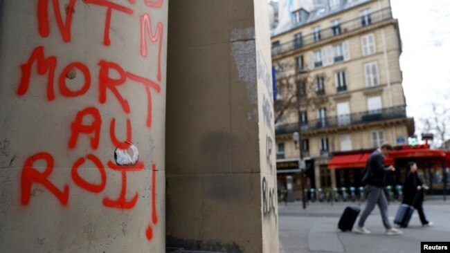 People walk past graffiti reading "Death to the King" the day after clashes during protests over French government's pension reform in Paris, March 24, 2023.