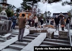 Orang-orang berdiri di dekat gerbang yang runtuh akibat gempa bumi di Kuil Onohiyoshi di Kanazawa, prefektur Ishikawa, Jepang 1 Januari 2024. (Foto: Kyodo via REUTERS)