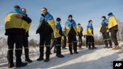 Newly-swapped Ukrainian prisoners of war, with Ukrainian national flags draped around their shoulders, are seen after an exchange for Russian POWs at an unspecified location on the Ukraine-Russia border, Jan. 31, 2024. 