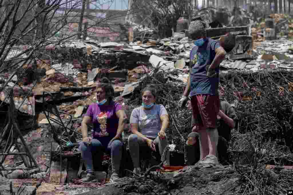 Residentes se toman un descanso mientras limpian los escombros de las casas quemadas después de que los incendios forestales alcanzaron su vecindario en Viña del Mar, Chile.