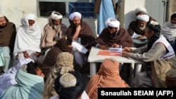 FILE - Afghan refugees deported from Pakistan wait to receive food aid by Red Cross Society in Kandahar on Jan. 24, 2024