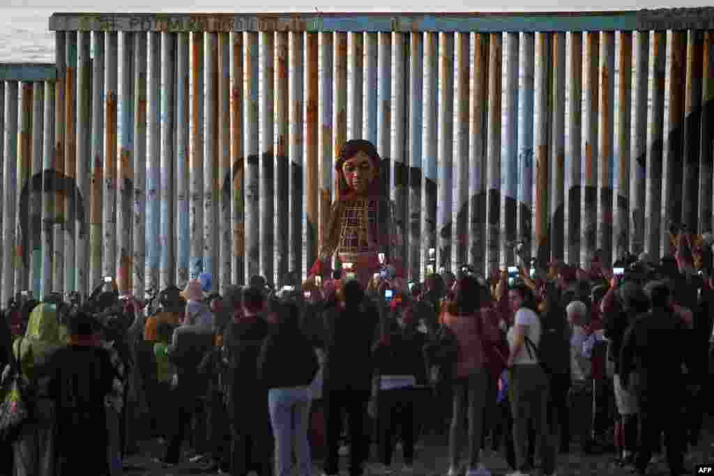 Little Amal, a 12-foot-tall puppet representing a 10-year-old Syrian refugee child, stands at the U.S.-Mexico border wall in Playas de Tijuana, Baja California, Mexico.&nbsp;Little Amal is visiting Tijuana within the framework of a journey across Mexico to raise awareness of the plight of refugees and migrants across the globe.