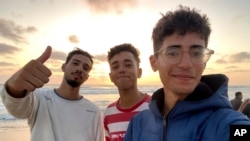 In this undated photo provided by Helmi Hirez, Mohamed (Medo) Halimy, left, and twin brothers Mohammed Hirez, center, and Helmi Hirez stand on a beach in Gaza. 