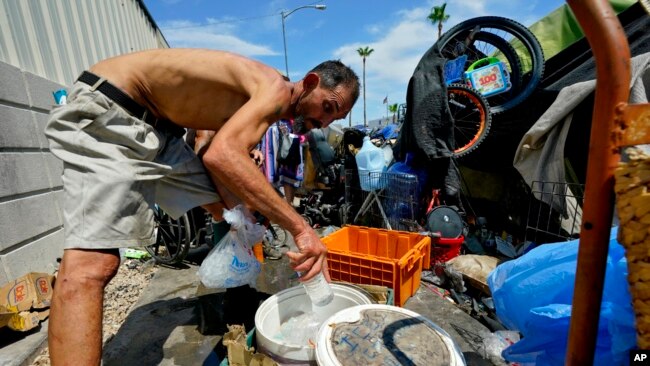 FILE - Kevin Hendershot pours ice into a bucket outside his tent in 'The Zone' homeless encampment, July 14, 2023, in downtown Phoenix.