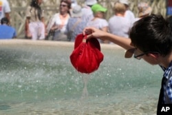 A child plunges his hat into a fountain in St. Peter's Square at Vatican City, July 16, 2023, as southern Europe experiences a heatwave.