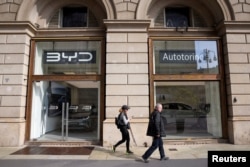 FILE - Orang-orang berjalan di depan ruang pamer dan dealer mobil BYD Auto dan Autotorino di Milan, Italia, 20 Maret 2024. (REUTERS/Claudia Greco)