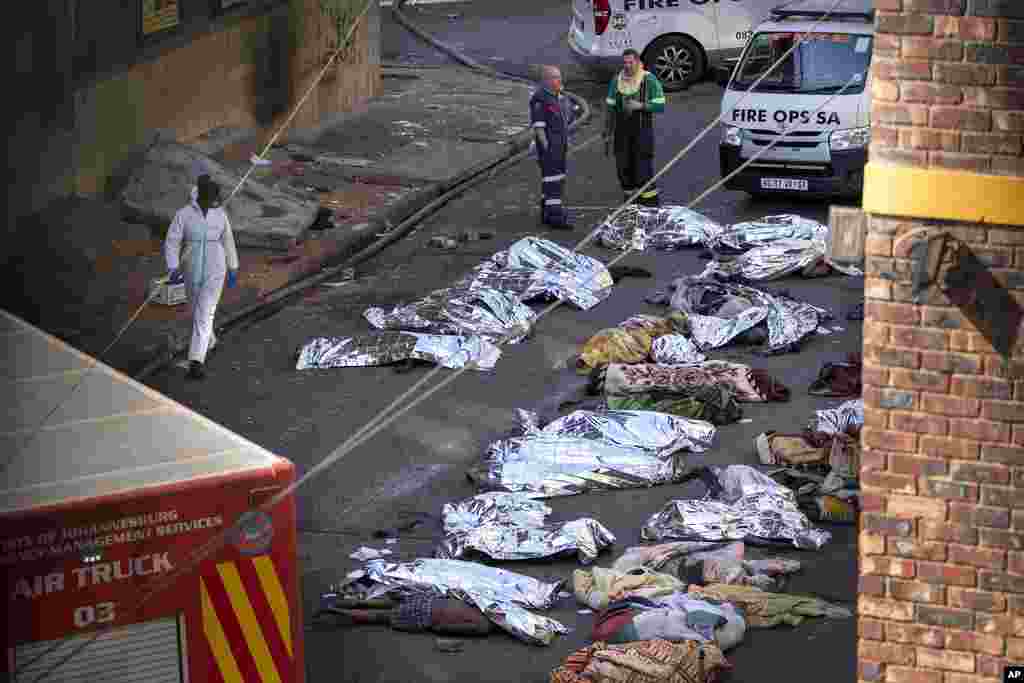 Medics stand by the covered bodies of victims of a deadly blaze in downtown Johannesburg, Thursday, Aug. 31, 2023.