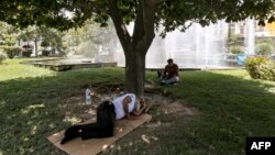 A man lies on a cardboard sheet spread as a mat on a lawn under the shade of a tree by a fountain while cooling off during a heat wave in Tehran on July 11, 2023.