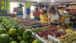 Una cliente revisa uvas, fresas y otras frutas exhibidas en un mercado de víveres en Maracaibo, en el occidente de Venezuela, mientras otros compradores se alistan para pagar sus pedidos, la mañana del jueves 13 de julio de 2023.