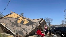 People sit in front of a damaged home, March 25, 2023 in Silver City, Miss. Emergency officials in Mississippi say dozens were killed by tornadoes that hit the state Friday night.