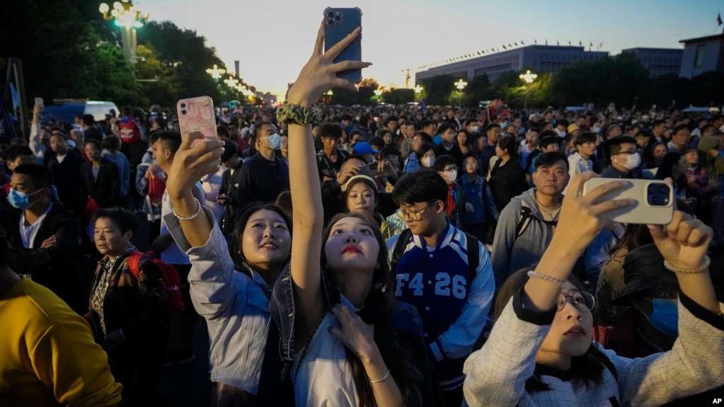 FILE - People take smartphone photos of the crowd on a street near Tiananmen Square as visitors gather to watch a flag-raising ceremony on the National Day in Beijing, Sunday, Oct. 1, 2023. (AP Photo/Andy Wong, File)