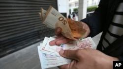 A man holds Algerian and European, top, bank notes Feb. 9, 2024, in Algiers, Algeria.