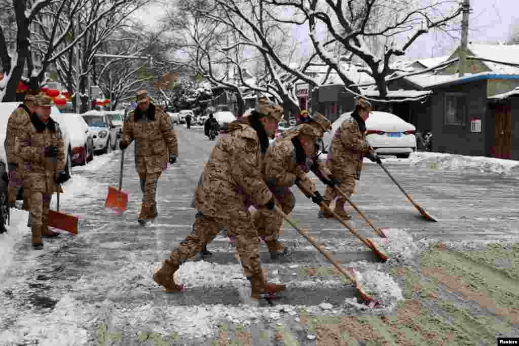 Paramilitary police officers shovel snow from a road following snowfall in Beijing, China.