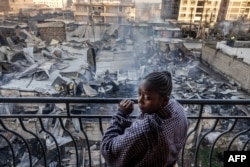 Seorang perempuan melihat dari balkon rumah-rumah dan toko-toko yang rusak berat, sehari setelah ledakan gas di kawasan Embakasi, Nairobi, 2 Februari 2024. (LUIS TATO / AFP)