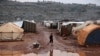 Seorang anak laki-laki asal Suriah tampak berjalan melalui area berlumpur di dekat tenda-tenda di kamp Kafr Arouk di Idlib, Suriah, pada 20 Desember 2021. (Foto: Reuters/Khalil Ashawi)