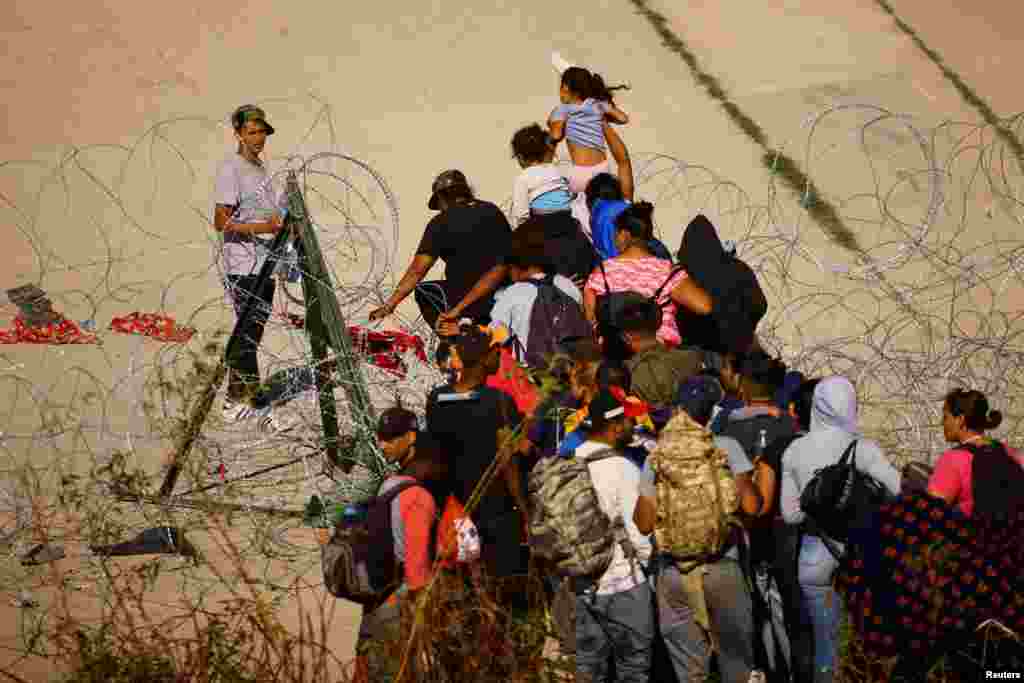 Migrants seeking asylum in the United States cross a razor wire fence near a border wall on the banks of the Rio Bravo River, on the border between the U.S. and Mexico, as seen from Ciudad Juarez, Mexico, Sept. 18, 2023. 