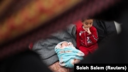 Seorang gadis duduk di samping Alma Al-Jadba, bayi perempuan kembar Palestina yang lahir dalam perang antara Israel dan Hamas di Rafah di Jalur Gaza selatan 17 Desember 2023. (Foto: REUTERS/Saleh Salem)