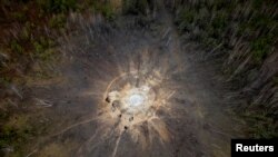People stand around a crater caused by a Russian missile strike in the village of Buda-Babynetska, outside Bucha, near Kyiv, Ukraine.