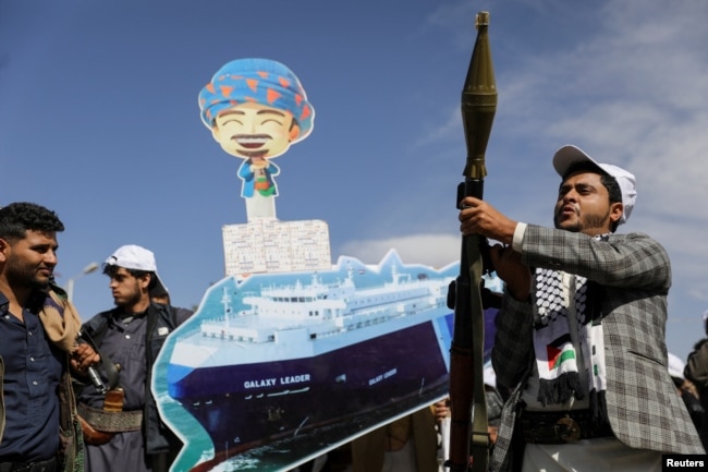 A Houthi follower holds a rocket launcher as others carry a cutout banner portraying the Galaxy Leader cargo ship that was seized by Houthis, during a parade as part of a "popular army" mobilization campaign, in Sanaa, Yemen, Feb. 7, 2024.