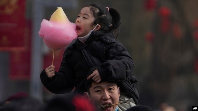A man carries his child on his shoulder as they visit the Longtan Park's temple fair during the second day of Lunar New Year celebrations in Beijing, Feb. 11, 2024.