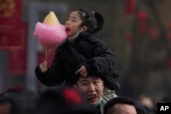 Seorang pria menggendong anaknya saat mengunjungi pameran di kuil Taman Longtan pada hari kedua perayaan Tahun Baru Imlek di Beijing, 11 Februari 2024. (AP Photo/Andy Wong)