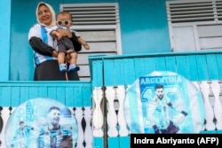 Seorang fans Lionel Messi, menggendong cucunya Muhammad Messi Pramudana sambil berpose di depan kediamannya yang dicat dengan warna bendera Argentina dan dihiasi poster Messi, di Polewali Mandar. (Foto: AFP/Indra Abriyanto)