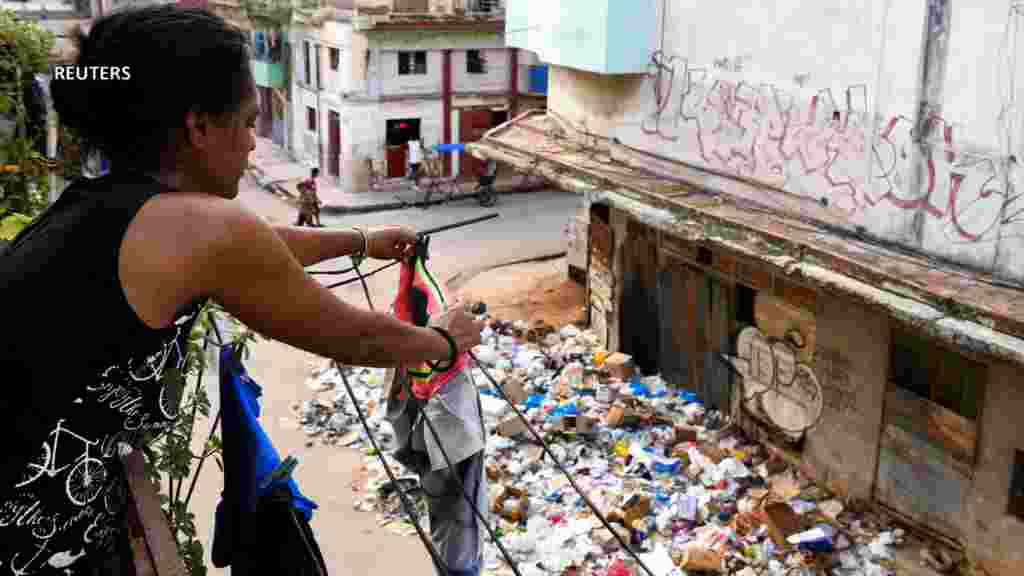 Una mujer cuelga la ropa en la ventana de su casa cerca de una pila de basura en una calle de La Habana, Cuba. (Reuters)