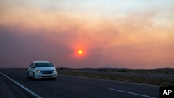 A car rides on the road to Roswell, New Mexico, as smoke from a wildfire partially blocks the sun near the village of Ruidoso, June 18, 2024.