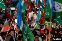 FILE - A portrait of former Prime Minister Imran Khan is seen amid flags of PTI and Jamat-e-Islami supporters at a joint protest demanding fair results outside election offices in Karachi, Feb. 10, 2024.
