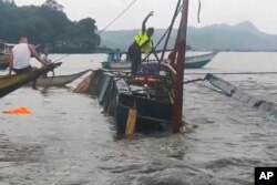 A man stands on a capsized passenger boat as they undergo rescue operations at Binangonan, Rizal province, east of Manila, Philippines, July 27, 2023. (Philippine Coast Guard via AP)