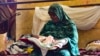 FILE - A woman, displaced by Sudan's conflict, cares for a baby at a makeshift shelter, in al-Hasahisa, south of Khartoum, July 8, 2023.
