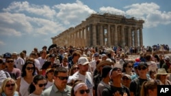 Atop the Acropolis ancient hill, tourists visit the Parthenon temple, background, in Athens, Greece, July 4, 2023.