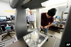 A Halter robot collects a finished piece for blood pressure pumps from a Mazak Integrex at Reata Engineering and Machine Works, Feb. 15, 2024, in Englewood, Colo.