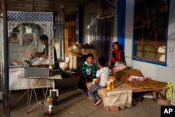 Seorang perempuan etnis Uighur bekerja sementara anak-anaknya bermain di Hotan, wilayah Xinjiang, China barat, 20 September 2018. (Foto: AP)