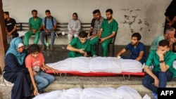 Para staf medis di Rumah Sakit Ahli Arab berduka di dekat jenazah rekan mereka yang dibungkus kafan yang terbunuh selama pemboman Israel di kamp pengungsi Shati, di lokasi rumah sakit di Kota Gaza (14/6).