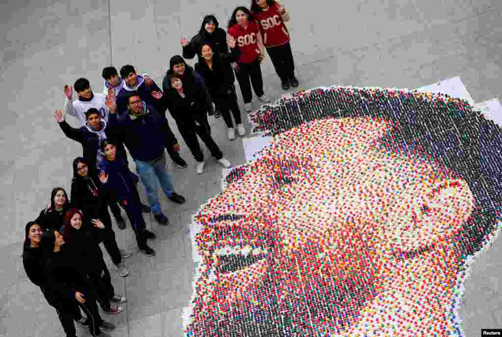 Art teacher Sebastian Ramirez waves with his students next to the mural they made with plastic bottle caps depicting Argentina&#39;s soccer superstar Lionel Messi, in Grand Bourg, on the outskirts of Buenos Aires.