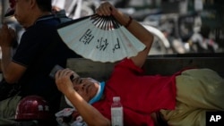 FILE - A man cools himself with a fan while browsing his phone on a sweltering day in Beijing, July 16, 2023.