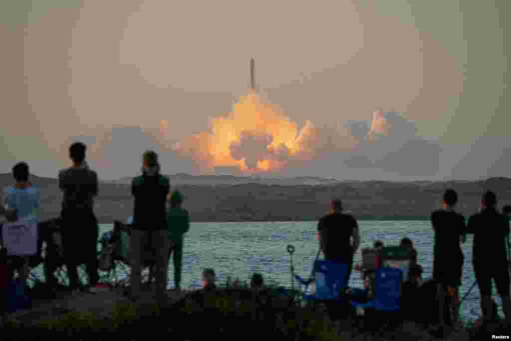 Луѓето гледаат како вселенското летало Starship од следната генерација на SpaceX на врвот на неговата моќна ракета Super Heavy се подига од лансирната рампа на компанијата Boca Chica за време на тест лет, како што се гледа од островот Јужен Падре, во близина на Браунсвил, Тексас, 18 ноември 2023 година.