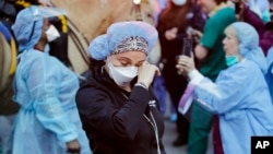 FILE - A medical worker reacts as police officers and pedestrians cheer medical workers outside NYU Medical Center in New York, April 16, 2020.