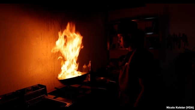 Un cocinero de comida china en Venezuela arroja un pedazo de pollo en un sartén hondo que agita en un intenso vaivén y que prende en fuego